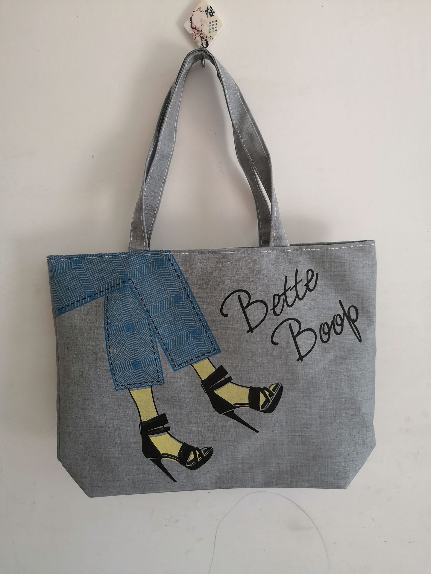 Gray canvas tote bag with blue patch panel and 'Bette Boop' script, side pocket