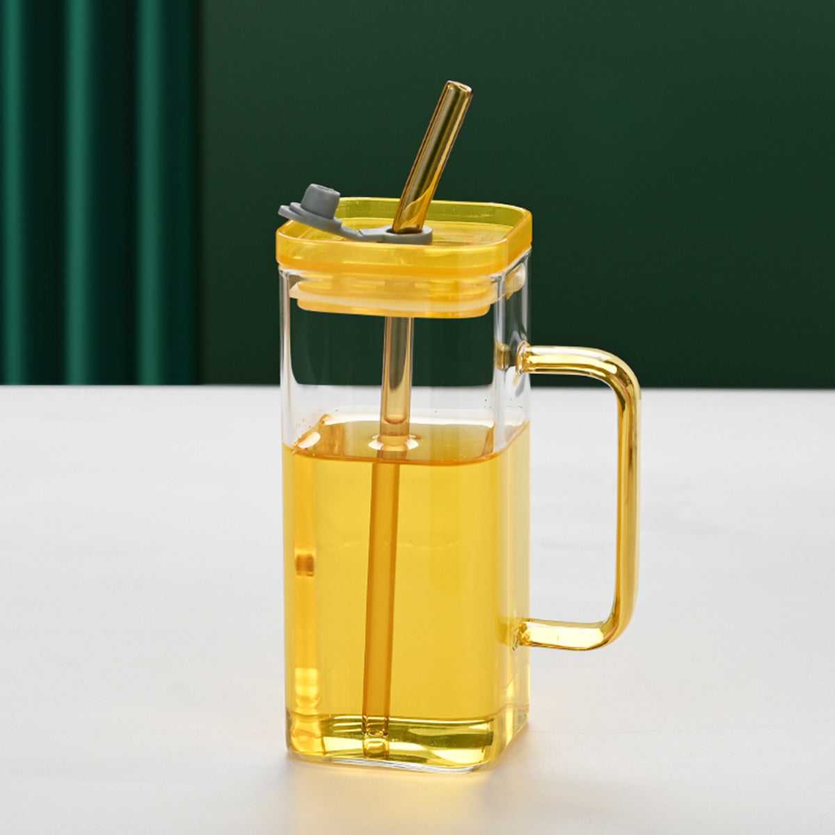 Clear square glass cup with yellow lid, gold straw, and yellow handle