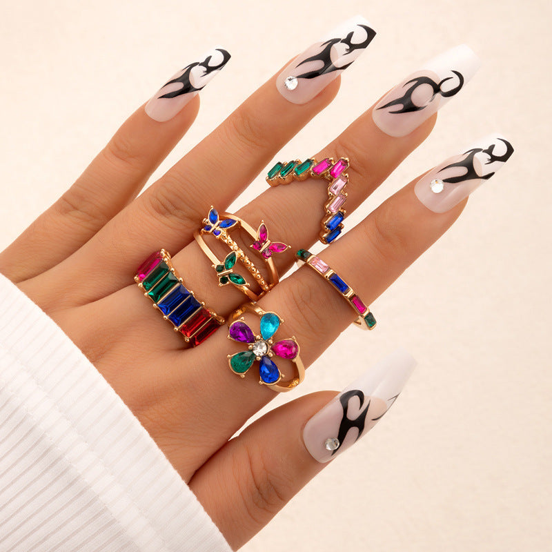 Gold-tone colorful crystal ring set on hand with floral, bar, and charm designs