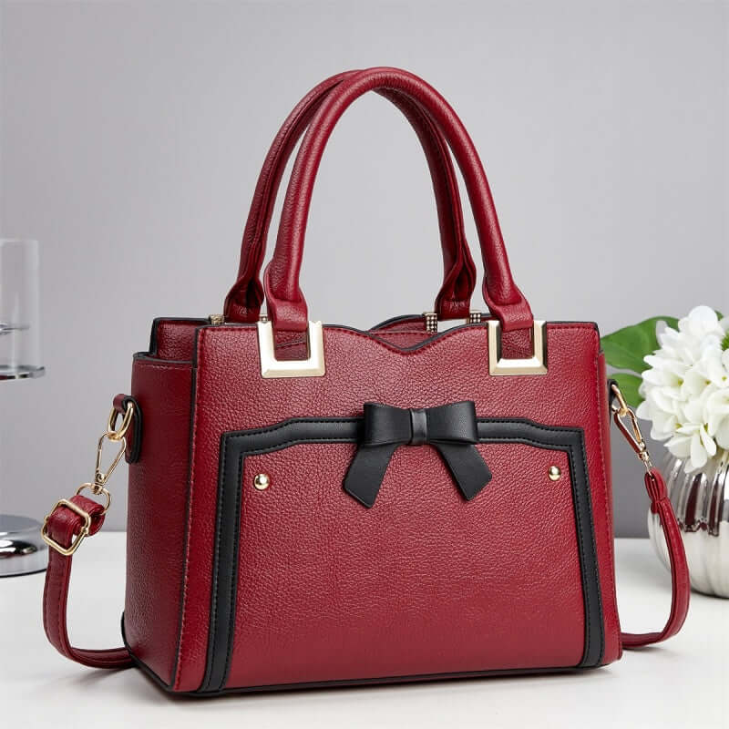 Red commuting shoulder bag with black bow front, gold-tone hardware, and crossbody strap