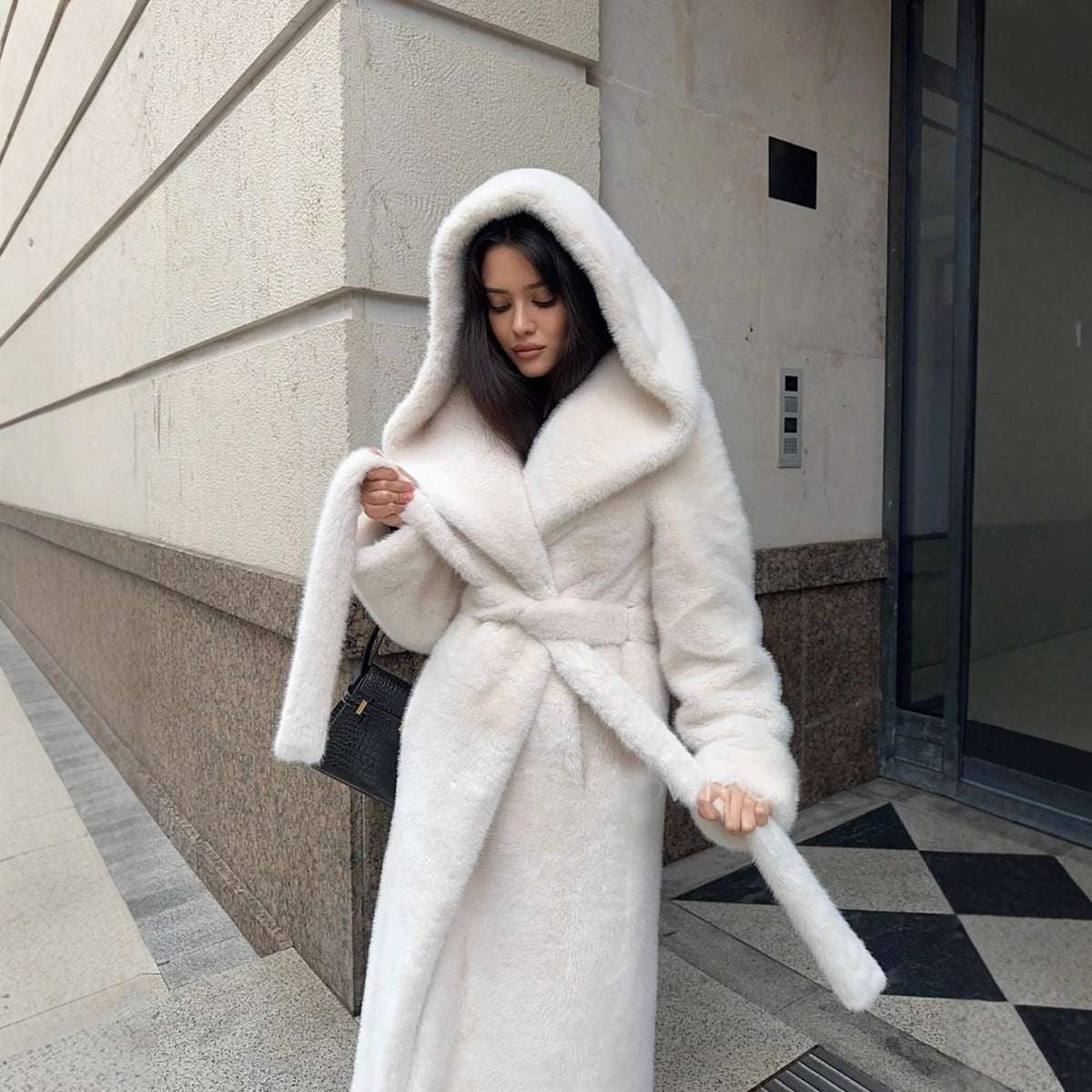 Woman wearing a white fur coat standing on a city street.