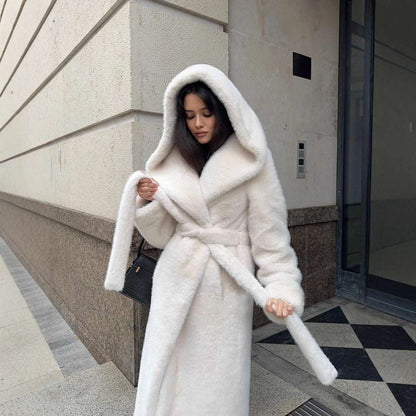 Woman wearing a white fur coat standing on a city street.