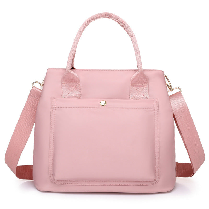 Pink fabric handbag with top handles, front pocket, and adjustable crossbody strap