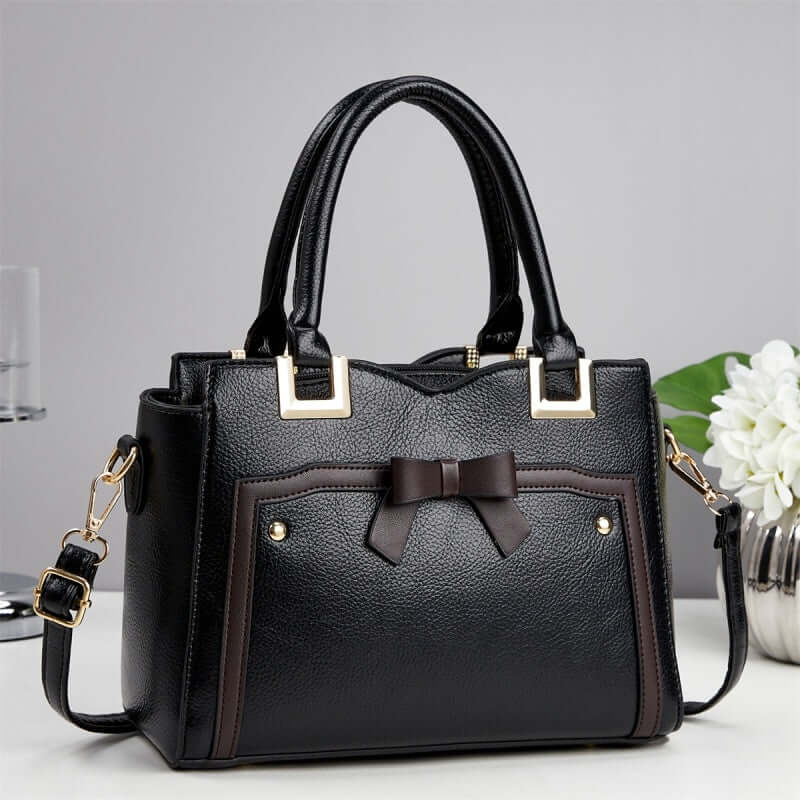 Black commuting shoulder bag with dark bow detail, brown accents, and crossbody strap