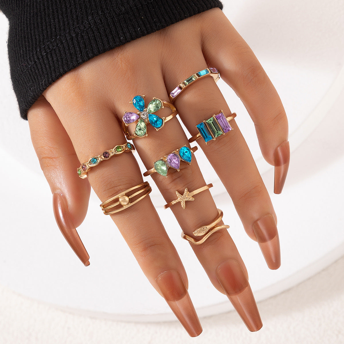 Gold-tone crystal ring set on hand, purple and green flower plus square gemstone band