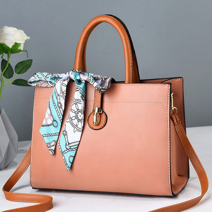Large pink crossbody tote with brown handles, blue patterned ribbon scarf, and metal clasp