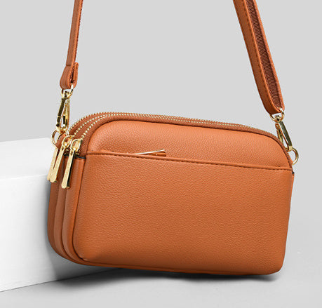 Tan one-shoulder crossbody bag with gold zipper and adjustable strap.