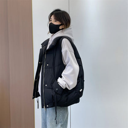 Person wearing a black puffer vest over a white hoodie against a neutral wall.