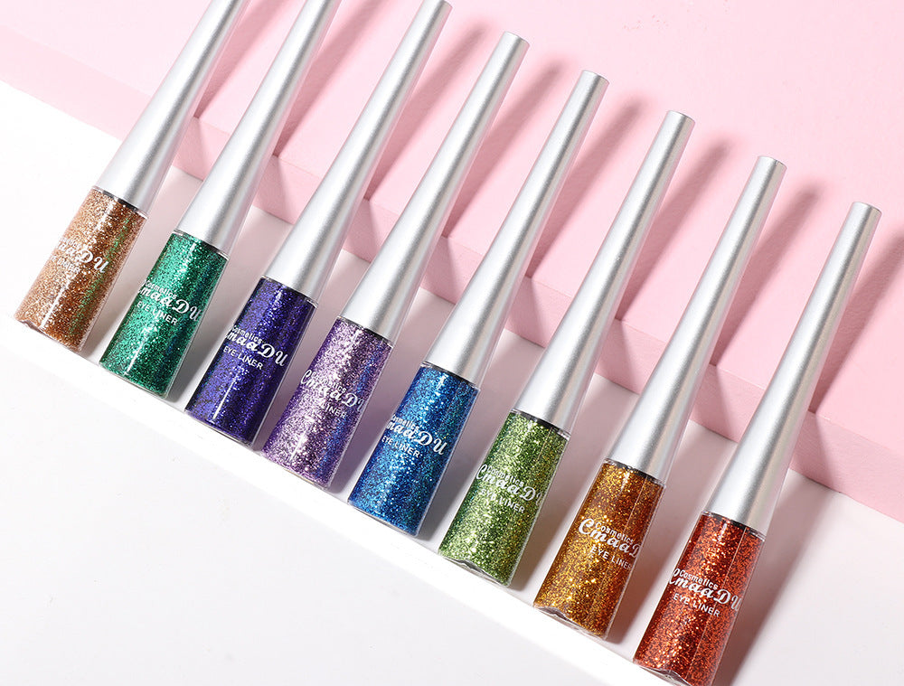 Set of glittery lip glosses with metallic applicators on a pink background
