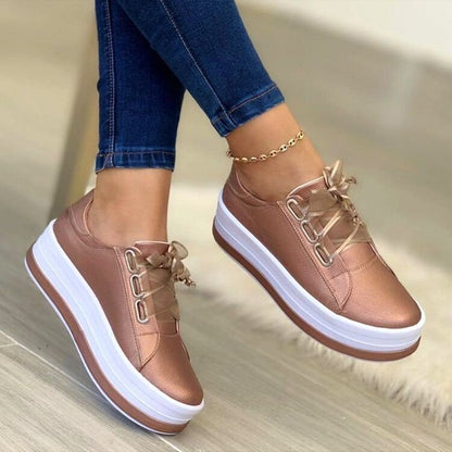 Rose gold sneakers with white soles worn with blue jeans on a neutral background
