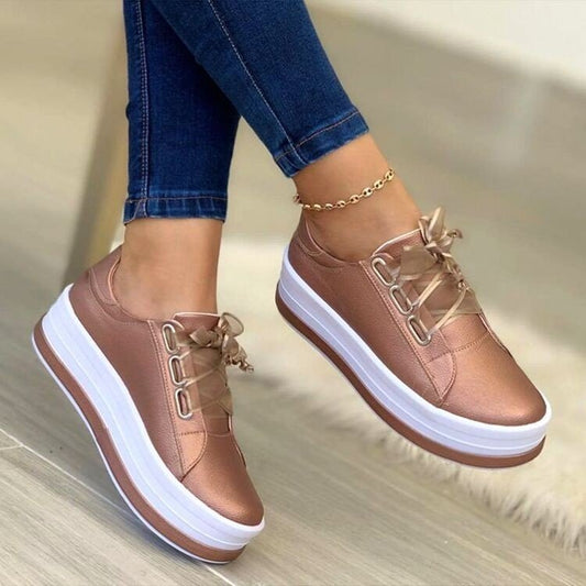Rose gold sneakers with white soles worn with blue jeans on a neutral background
