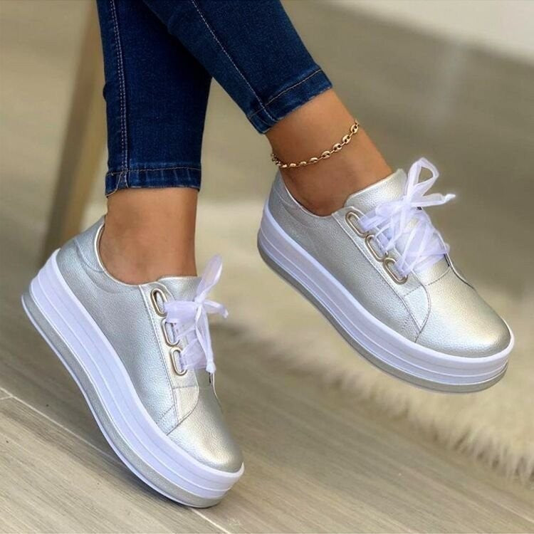 White sneakers with a platform sole worn with blue jeans on a neutral background