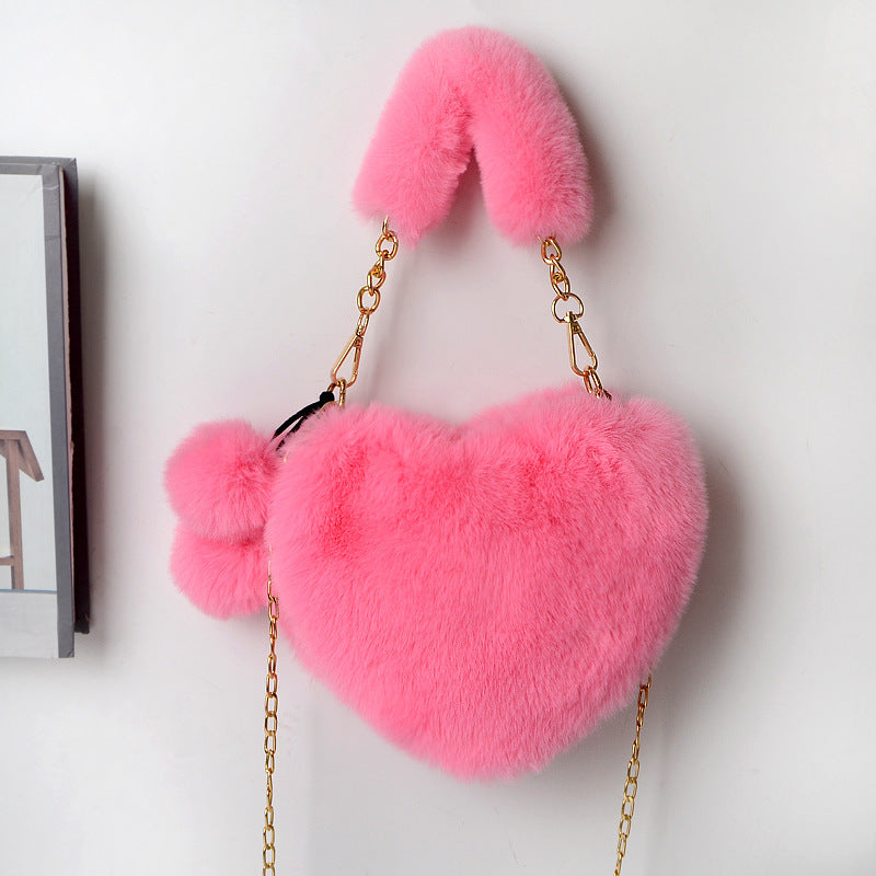 Pink plush heart shoulder bag with gold chain and fuzzy pom-pom charm.