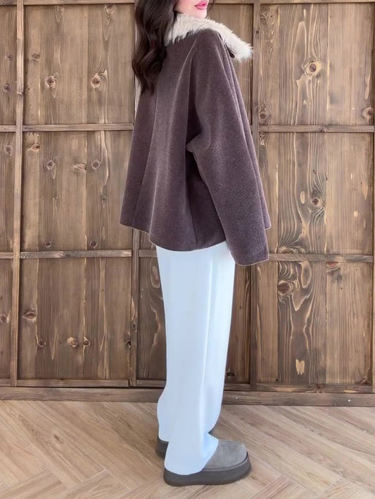 Person wearing a brown coat with fur trim against a wooden background