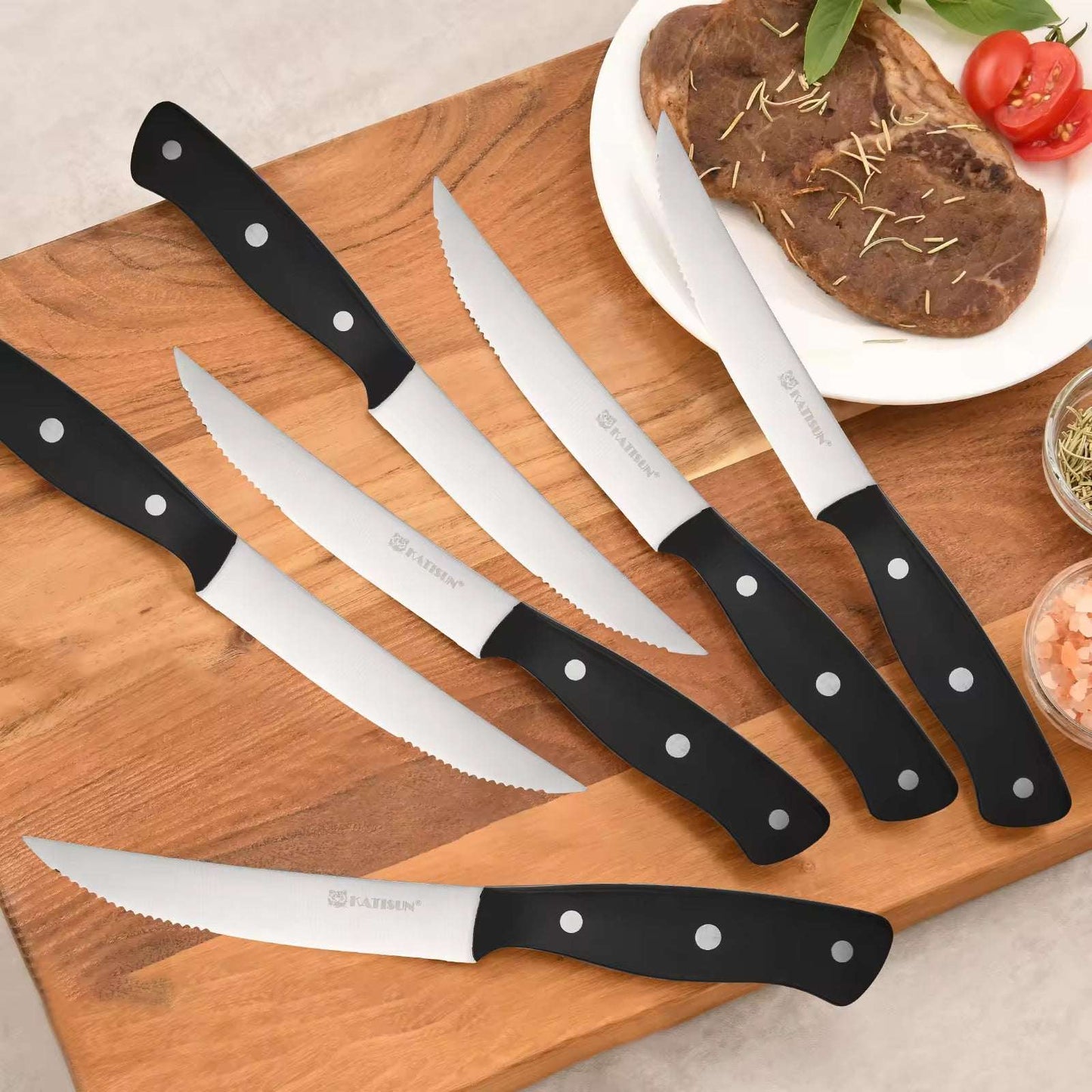 Set of serrated steak knives with black handles on a wooden board with food
