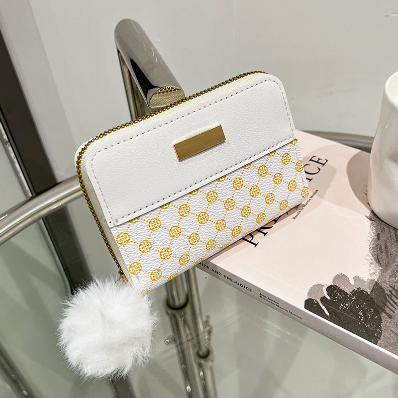 White short wallet with gold clasp, yellow patterned band, and fuzzy pom-pom