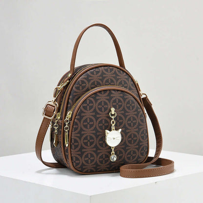 Brown patterned mini shoulder handbag with top handle, long strap, and dangling heart charm