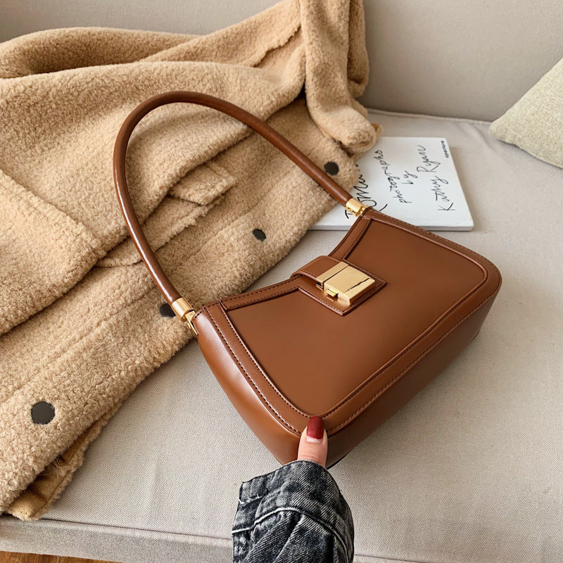 A woman sitting with crossed legs, wearing a beige sweater, black pants, and black shoes, carrying a black shoulder bag with a gold clasp.