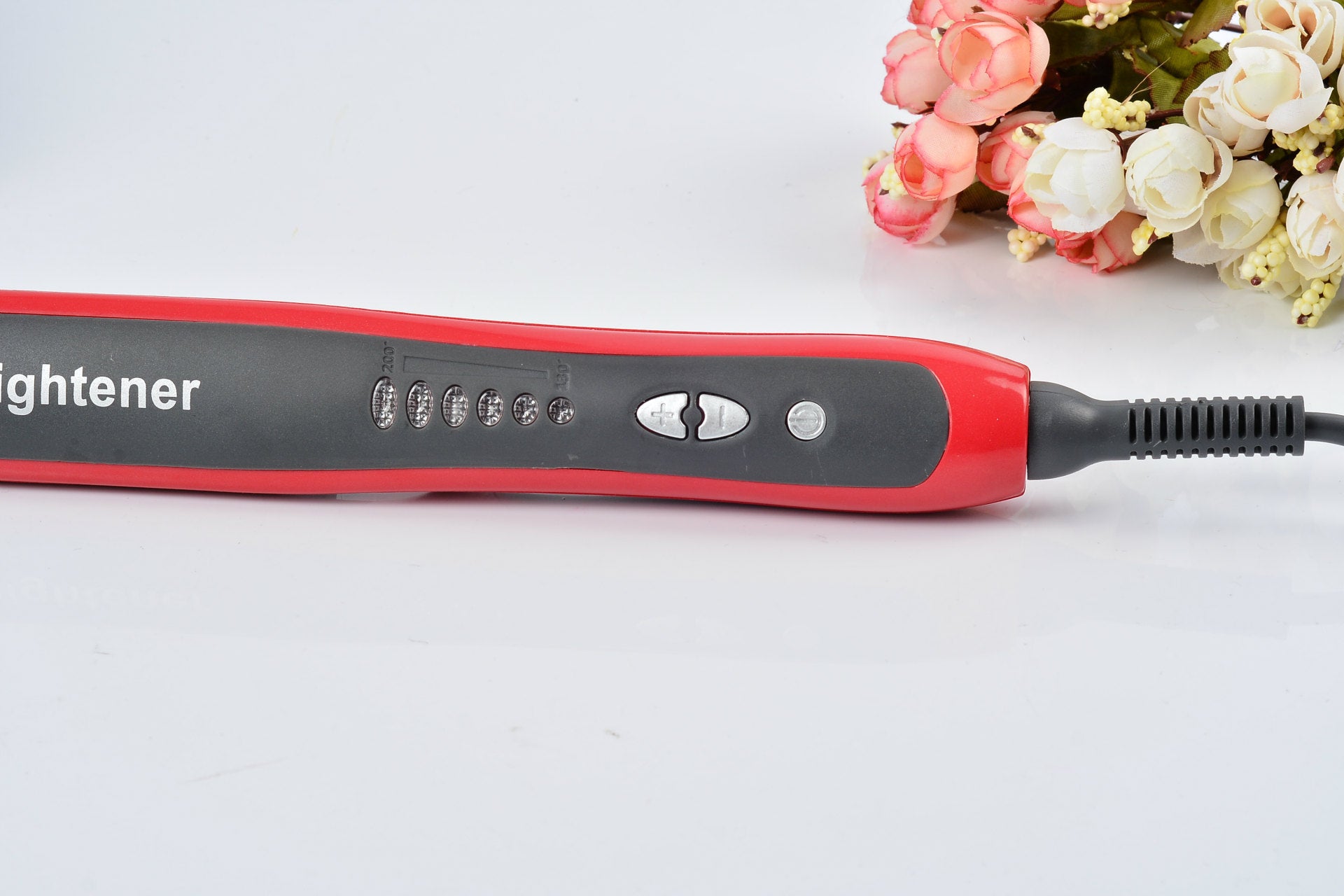 Red and black hair straightener on a white background with flowers.