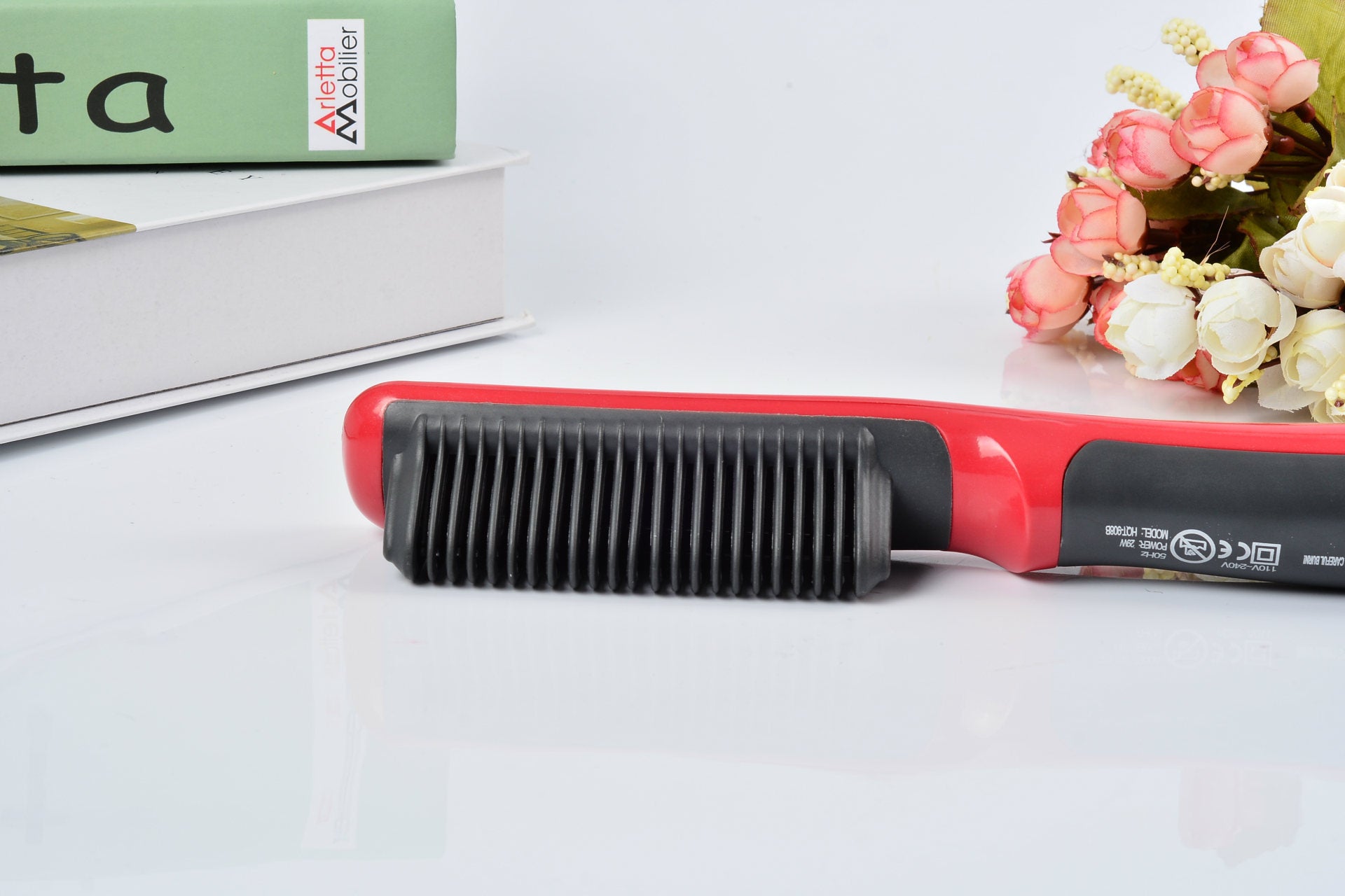 Red and black hair straightener on a white surface with a blurred background