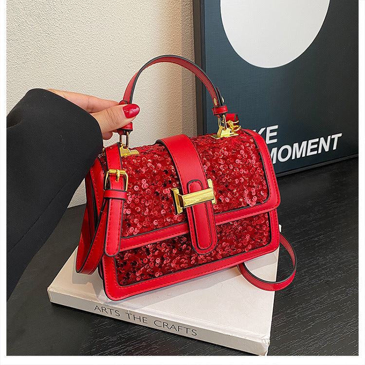 Red sequined shoulder bag with flap, gold buckle closure, and red crossbody strap