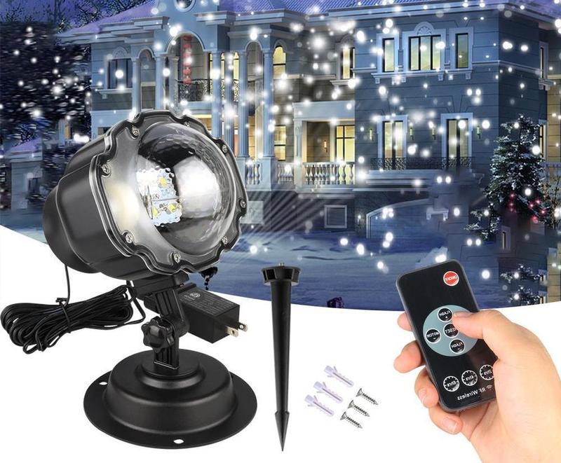 Outdoor Christmas light projector with remote control in front of a house with holiday decorations.
