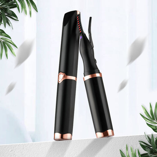 Black and rose gold eyelash curler on a light background with green leaves