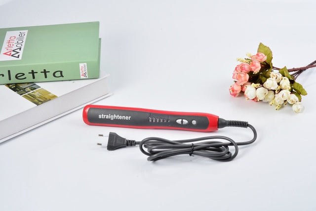 Hair straightener on a white surface with flowers and a magazine in the background